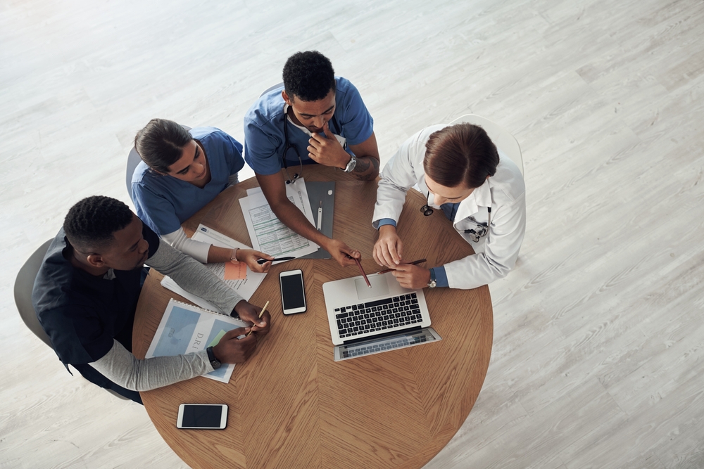 group of 4 doctors sitting around a circular table having a discussion 