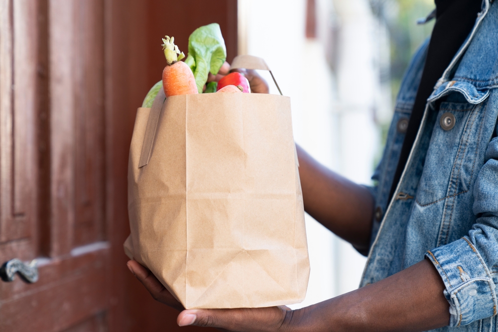 a man dropping off a brown paper bag of groceries at a front door